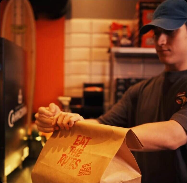 Colaborador embalando pedido King Pizza Looong com a mensagem Eat The Rules