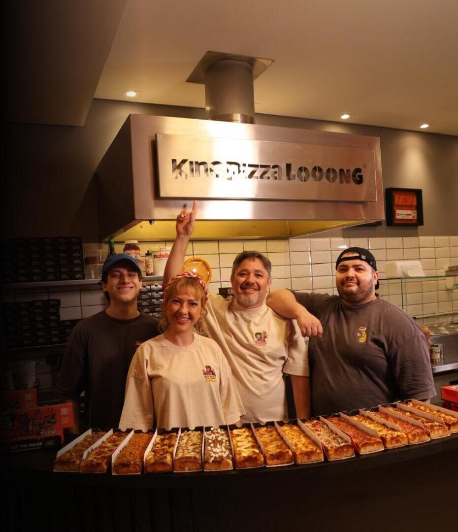 Equipe King Pizza Looong atrás do balcão com dezenas de pizzas Looong